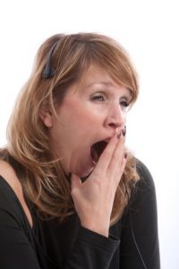 Female receptionist with headset yawning very wide; she may be suffering from sleep disorders.